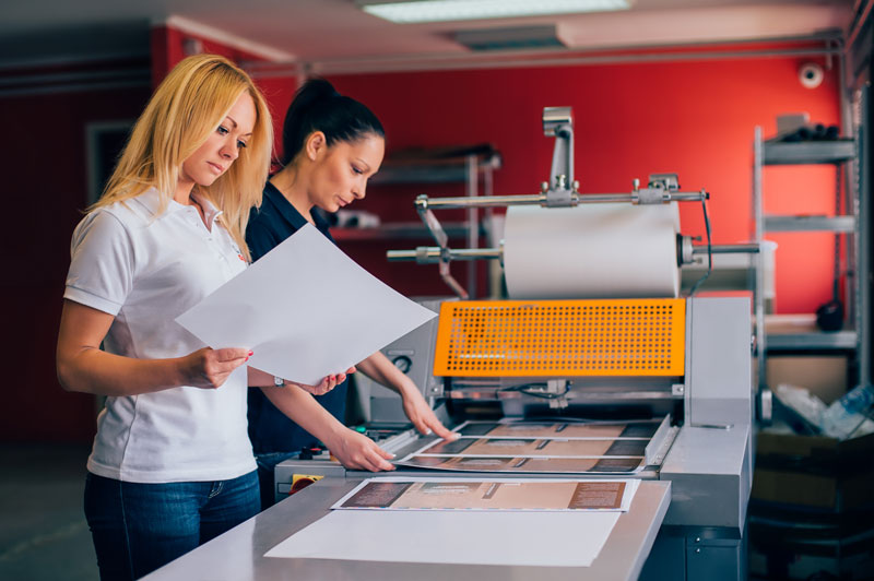 Two women checking the printer output in a printing workshop